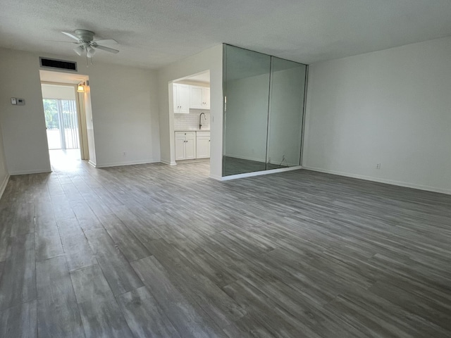 unfurnished living room featuring a textured ceiling, dark wood-style flooring, visible vents, baseboards, and a ceiling fan