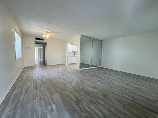 unfurnished living room with dark wood-style floors, visible vents, a ceiling fan, a textured ceiling, and baseboards