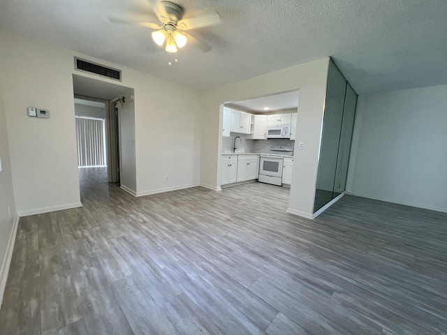 unfurnished living room with a textured ceiling, a sink, visible vents, baseboards, and light wood finished floors