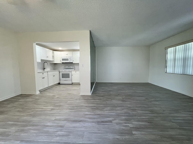 unfurnished living room featuring light wood-type flooring, a textured ceiling, baseboards, and a sink