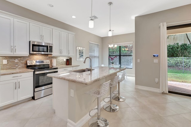 kitchen featuring stainless steel appliances, a sink, white cabinetry, and decorative light fixtures