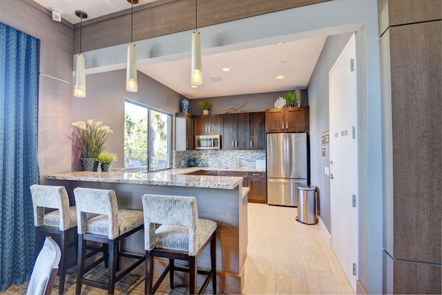 kitchen with light stone counters, a breakfast bar, decorative light fixtures, stainless steel appliances, and a peninsula