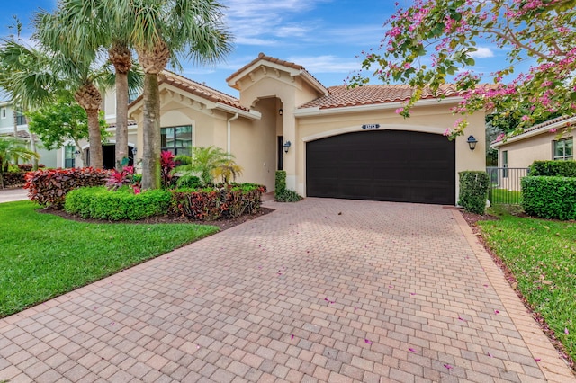 mediterranean / spanish-style home featuring decorative driveway, stucco siding, an attached garage, a front yard, and fence