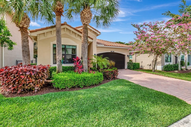 mediterranean / spanish home featuring decorative driveway, stucco siding, a garage, a tiled roof, and a front lawn