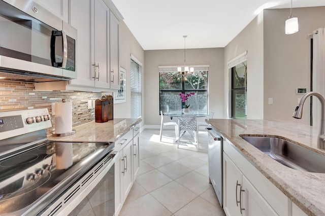 kitchen featuring stainless steel appliances, pendant lighting, a sink, and light stone counters