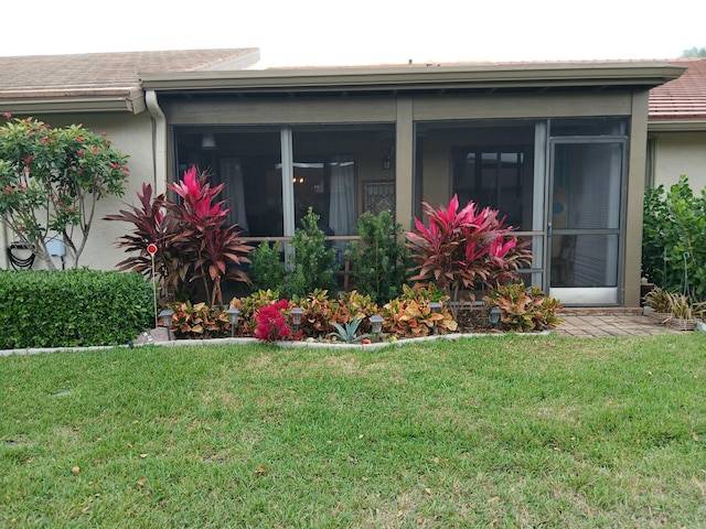 exterior space featuring a sunroom, a yard, and stucco siding