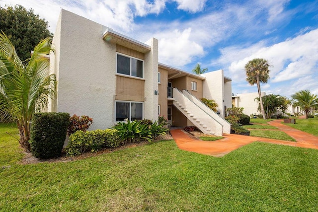 exterior space featuring stairway, a lawn, and stucco siding