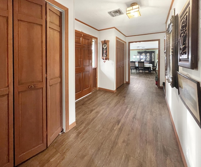 corridor with ornamental molding, dark wood-style flooring, visible vents, and baseboards