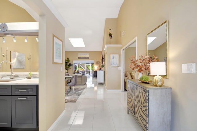 hallway with baseboards, visible vents, lofted ceiling with skylight, a sink, and light tile patterned flooring