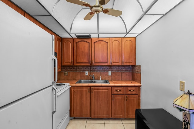 kitchen with light tile patterned floors, white appliances, a sink, tile counters, and tasteful backsplash