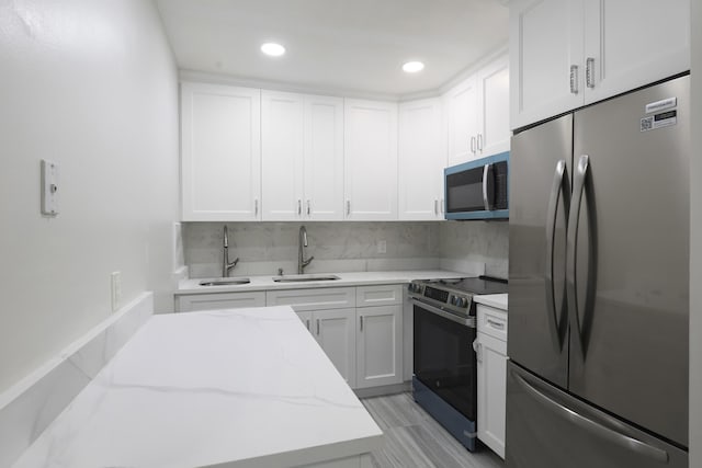 kitchen featuring stainless steel appliances, tasteful backsplash, white cabinetry, a sink, and light stone countertops