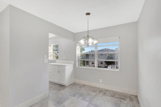 unfurnished dining area featuring a healthy amount of sunlight, baseboards, and an inviting chandelier