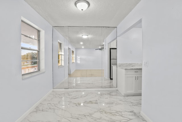 corridor featuring a textured ceiling, marble finish floor, and baseboards