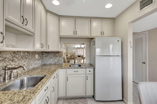 kitchen with tasteful backsplash, visible vents, freestanding refrigerator, a sink, and light stone countertops