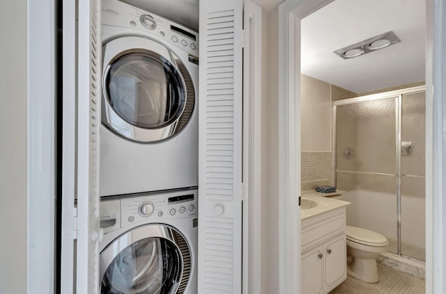 clothes washing area featuring stacked washer and clothes dryer, tile walls, and laundry area