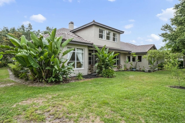 back of property featuring stucco siding, a lawn, a chimney, and a tiled roof