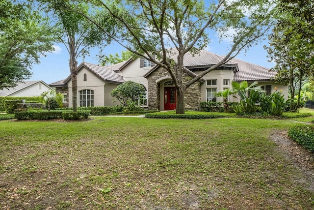 view of front of property with a front yard, a tiled roof, stone siding, and stucco siding