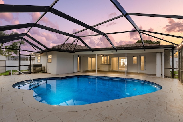 pool at dusk featuring ceiling fan, glass enclosure, a patio area, and an outdoor pool