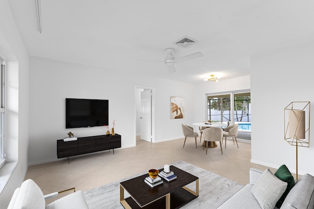 living area with light tile patterned floors, a ceiling fan, visible vents, and baseboards