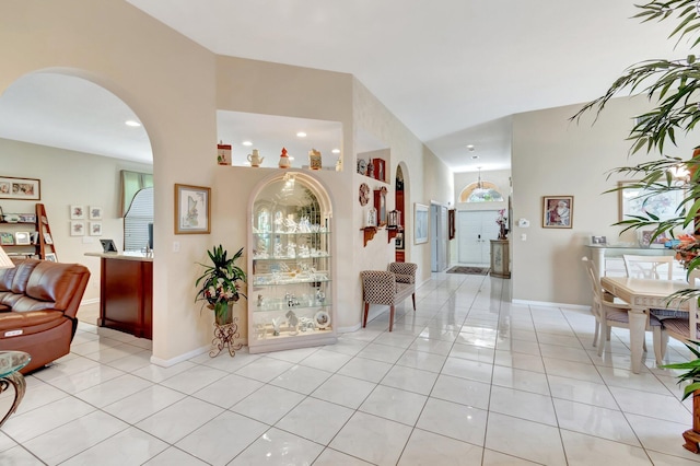 corridor with arched walkways, light tile patterned flooring, and baseboards