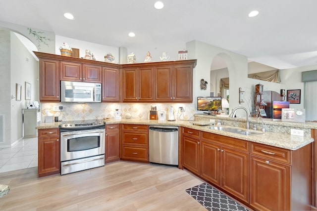 kitchen with appliances with stainless steel finishes, a peninsula, light stone countertops, a sink, and backsplash