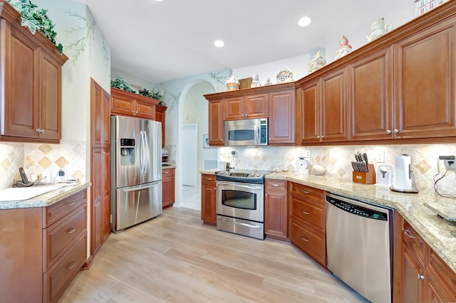 kitchen with tasteful backsplash, light wood-style flooring, light stone counters, brown cabinets, and stainless steel appliances