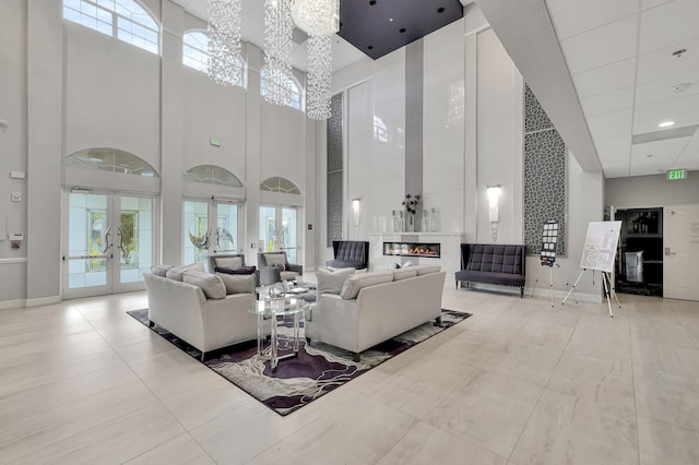 living room with french doors, a notable chandelier, a fireplace, a towering ceiling, and baseboards