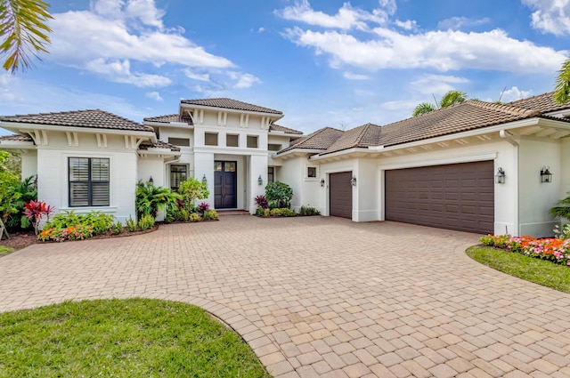 view of front facade with a garage, a tiled roof, decorative driveway, and stucco siding