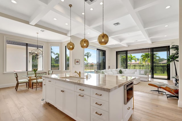 kitchen with visible vents, light wood-style flooring, light stone counters, open floor plan, and a sink