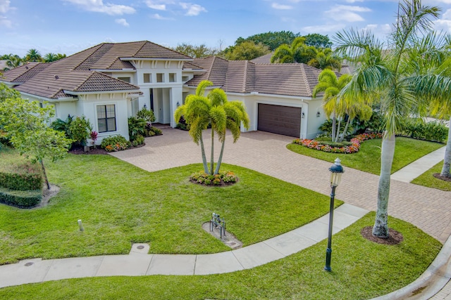 mediterranean / spanish house with a garage, decorative driveway, a tiled roof, and a front lawn