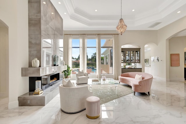 living room with a tile fireplace, a towering ceiling, marble finish floor, a raised ceiling, and crown molding