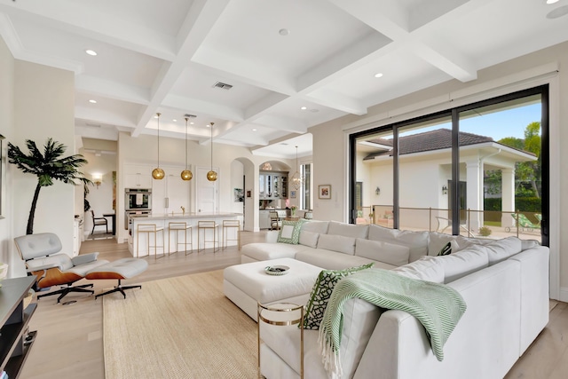 living area featuring arched walkways, visible vents, coffered ceiling, light wood-style floors, and beam ceiling