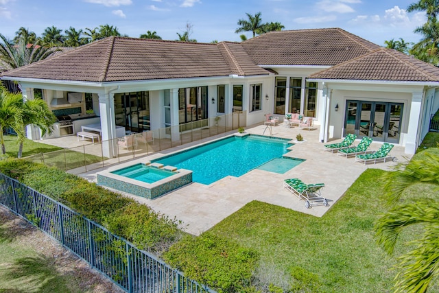 back of house featuring a tile roof, a patio, a pool with connected hot tub, an outdoor kitchen, and fence private yard