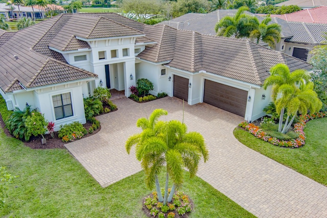 mediterranean / spanish-style house with decorative driveway, an attached garage, a tile roof, and a front yard