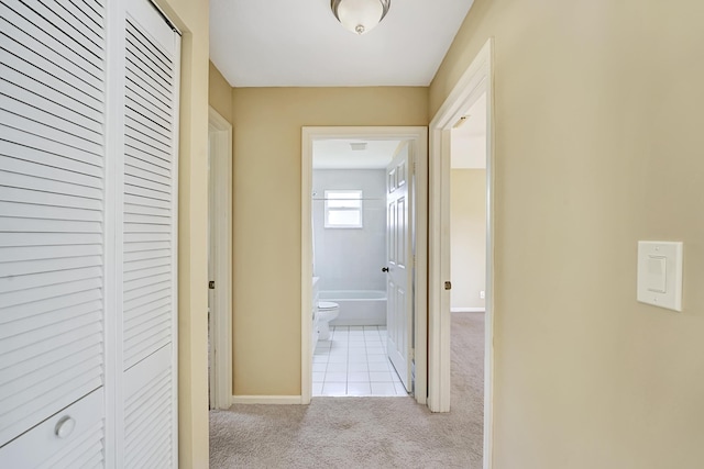 corridor with baseboards, light tile patterned floors, and light colored carpet