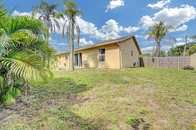 rear view of property with fence, a lawn, and stucco siding