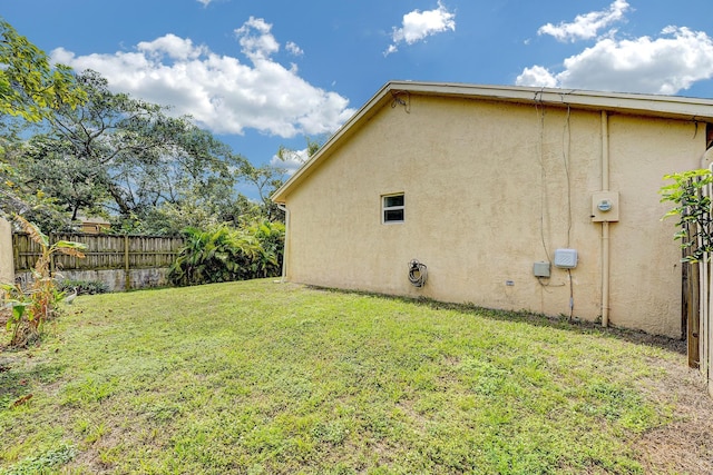 view of side of home with a yard, fence, and stucco siding