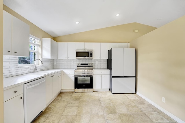 kitchen with white cabinets, vaulted ceiling, stainless steel appliances, light countertops, and a sink