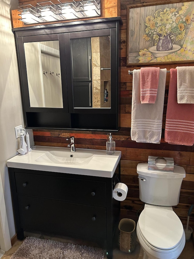 half bathroom featuring vanity, toilet, and wood walls