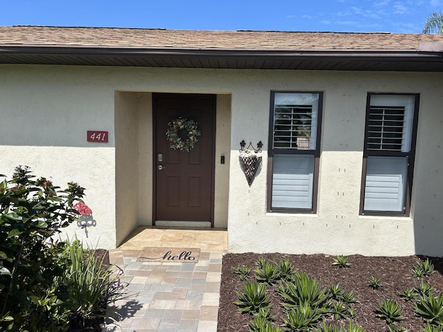 view of exterior entry with a shingled roof and stucco siding