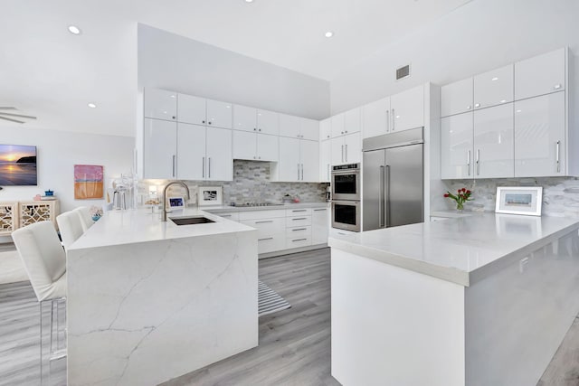 kitchen with a peninsula, stainless steel appliances, a kitchen bar, white cabinetry, and a sink