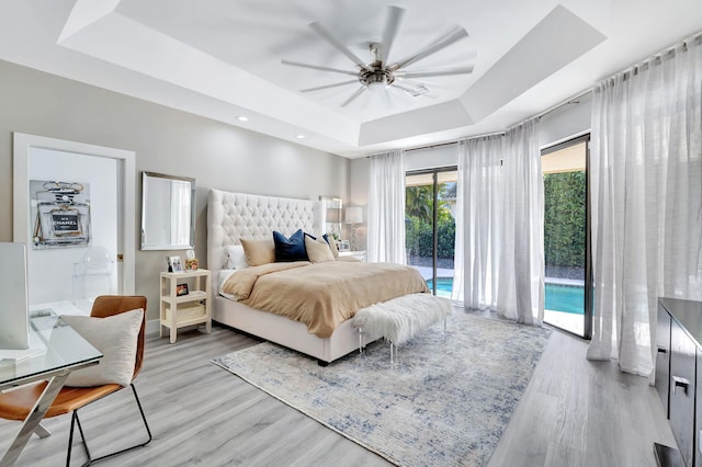 bedroom with access to exterior, a tray ceiling, ceiling fan, and light wood finished floors