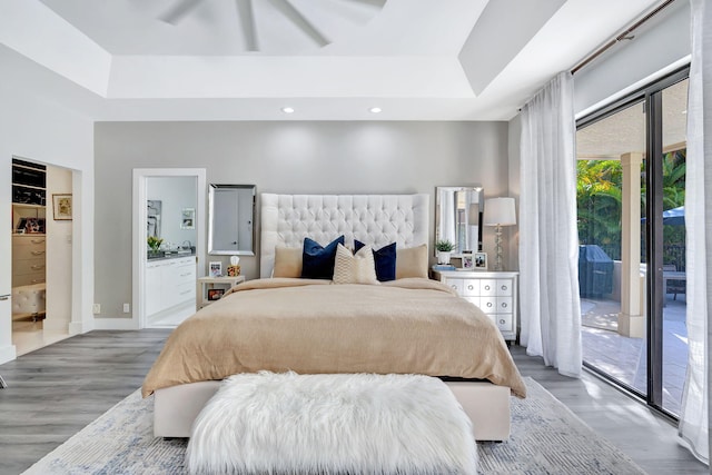 bedroom featuring access to exterior, a tray ceiling, and wood finished floors