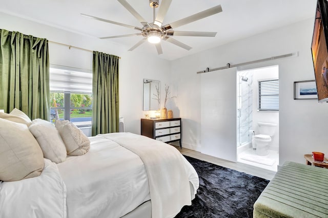 bedroom with a ceiling fan, dark wood finished floors, connected bathroom, and a barn door