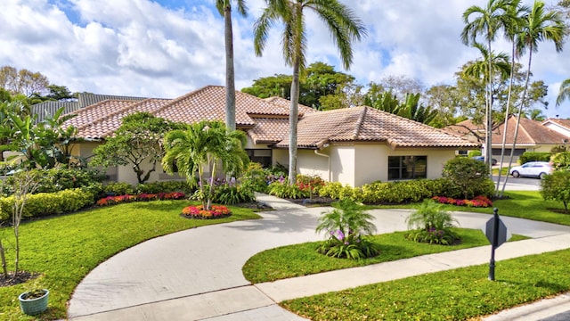 mediterranean / spanish-style house with stucco siding, a tile roof, and a front yard