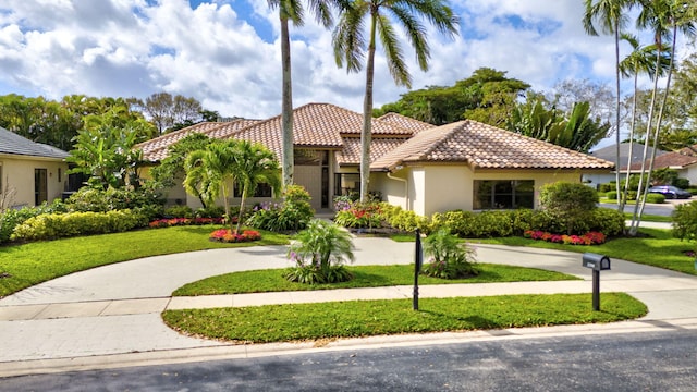 mediterranean / spanish-style home featuring driveway, a tile roof, a front lawn, and stucco siding