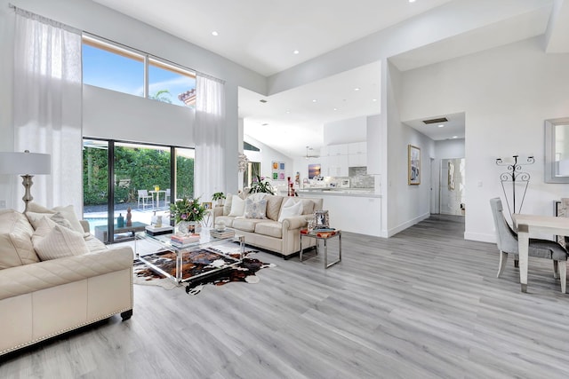 living room with light wood-type flooring, a high ceiling, baseboards, and recessed lighting