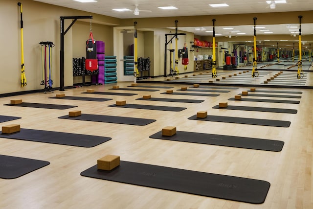 gym featuring a paneled ceiling, baseboards, and wood finished floors