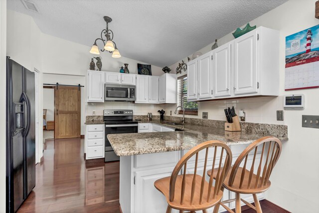 kitchen featuring a barn door, a peninsula, hanging light fixtures, stainless steel appliances, and white cabinetry
