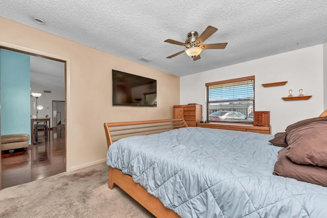 bedroom with baseboards, visible vents, a ceiling fan, light colored carpet, and a textured ceiling